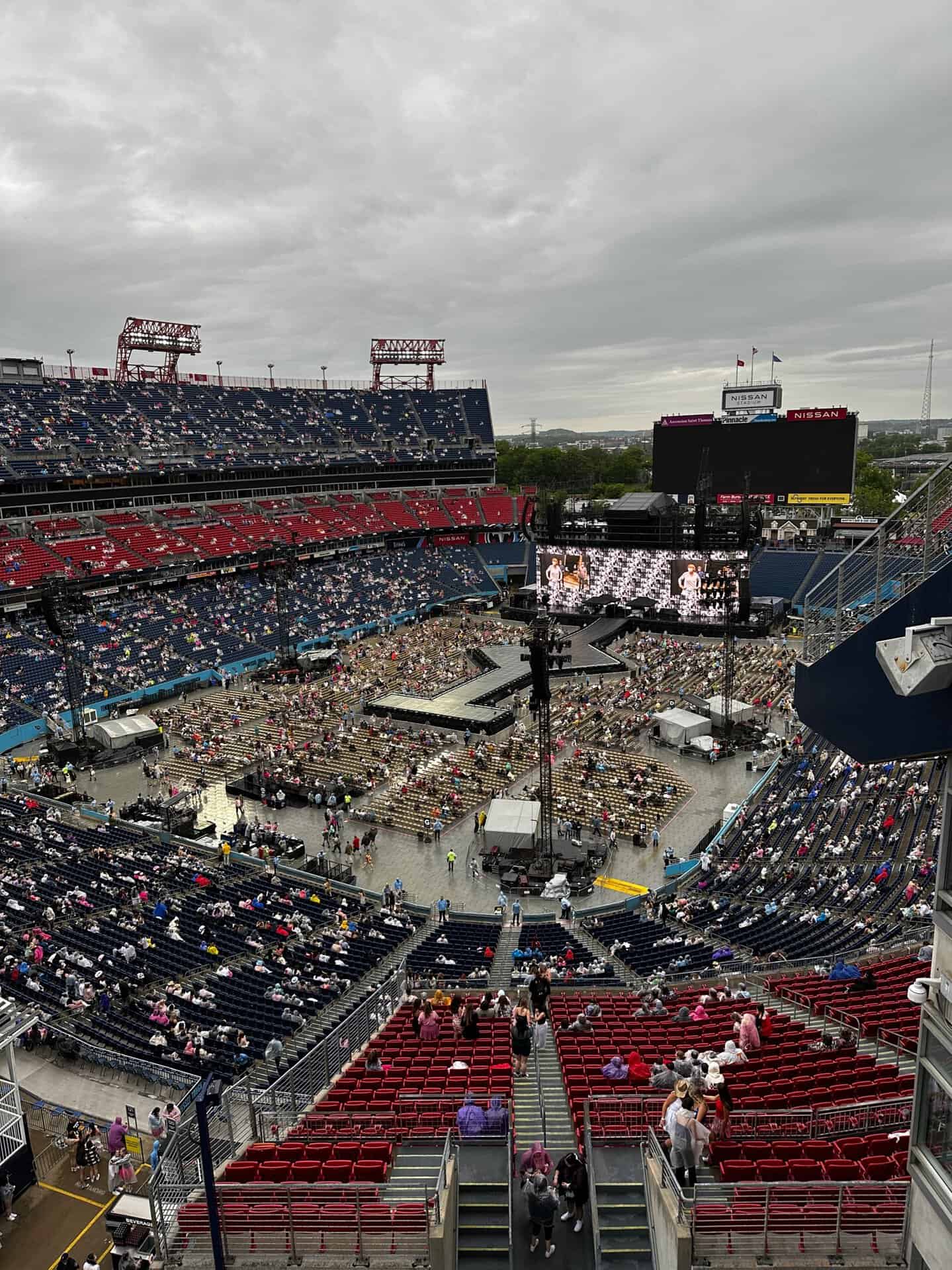 A large stadium in Nashville features a stage set up in the center, with a sparse crowd occupying the red and blue seats beneath a cloudy sky.