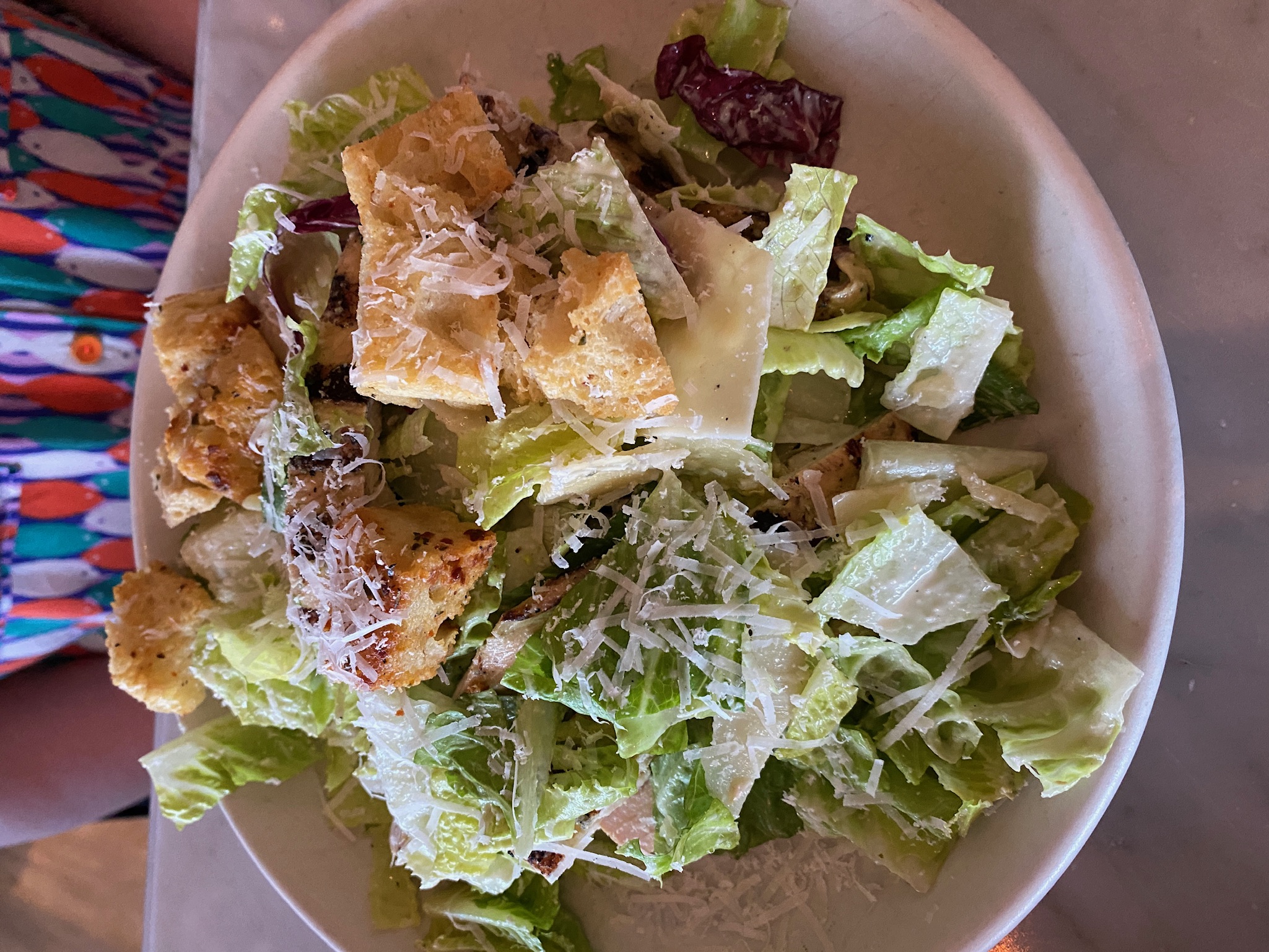 A plate of Caesar salad with romaine lettuce, croutons, and grated Parmesan cheese on a white dish.