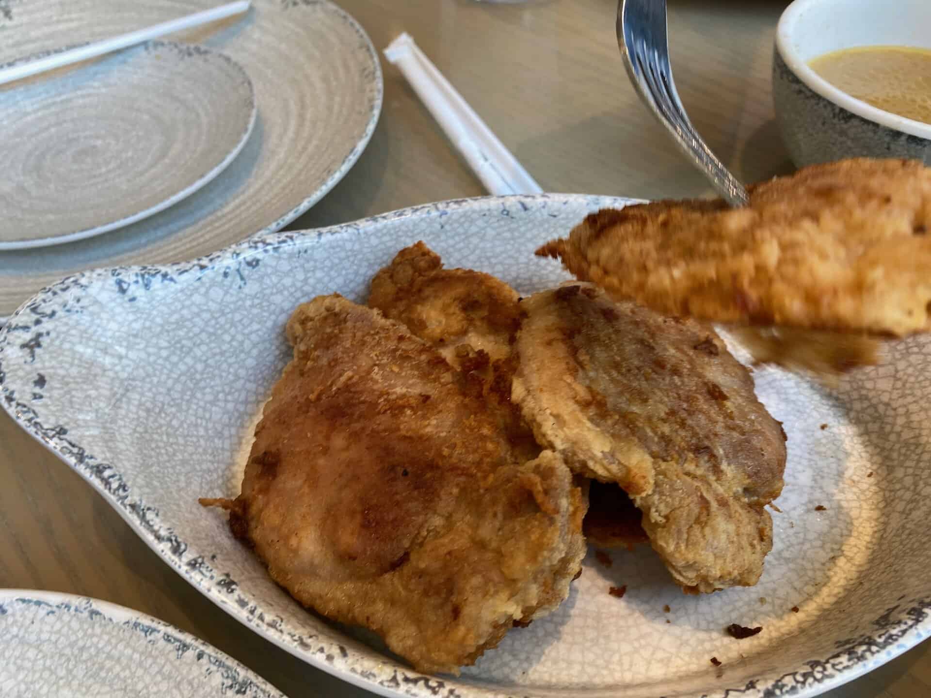 A plate of fried dumplings on a textured dish, with a fork lifting one. Plates and a bowl of sauce are in the background.