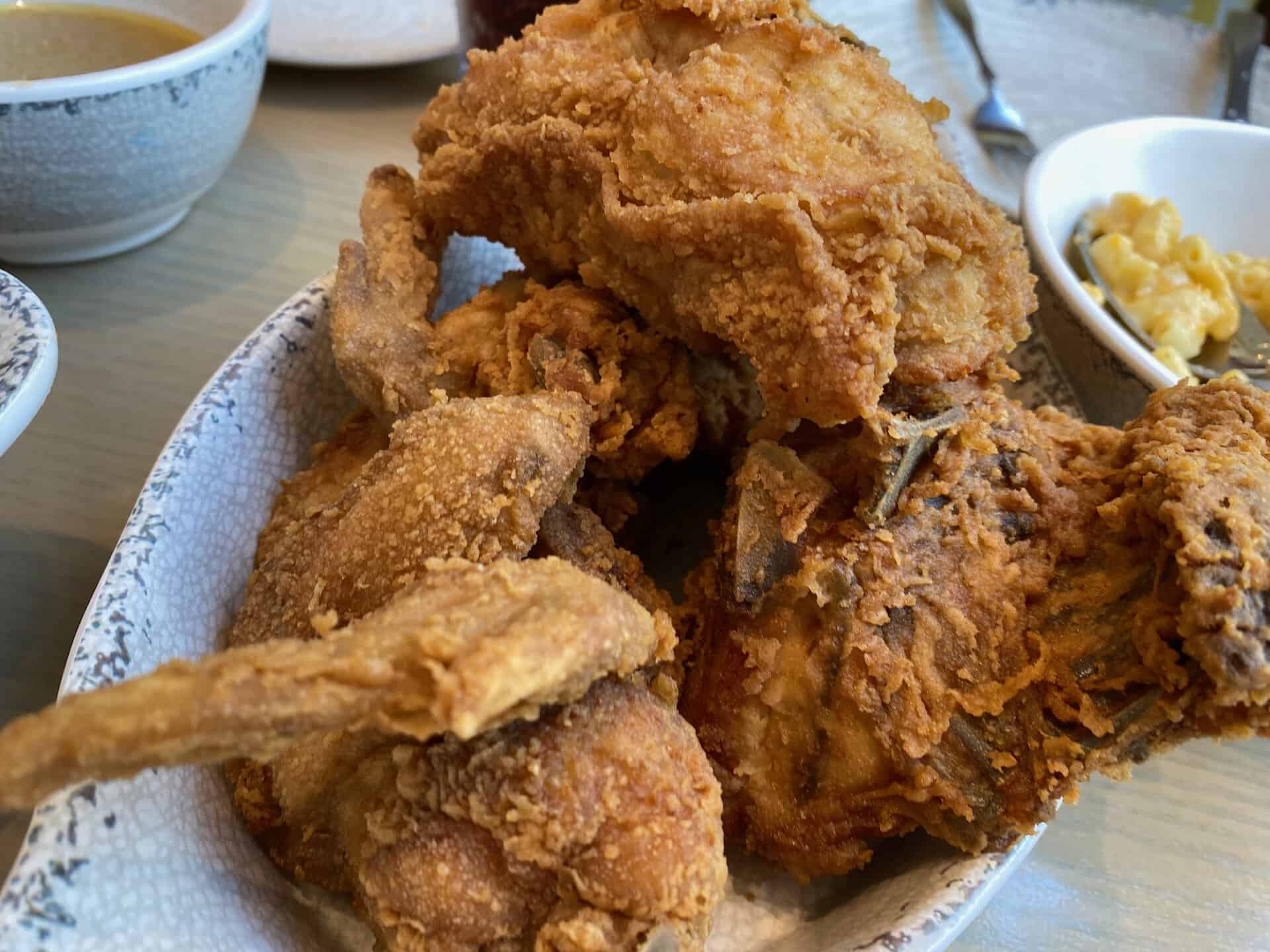 A plate filled with pieces of crispy fried chicken, accompanied by a small dish of macaroni and cheese in the background.