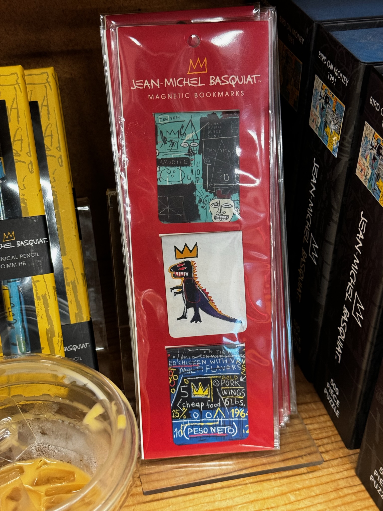 A package of Jean-Michel Basquiat magnetic bookmarks featuring three different artworks, displayed on a wooden shelf next to other Basquiat-themed items.