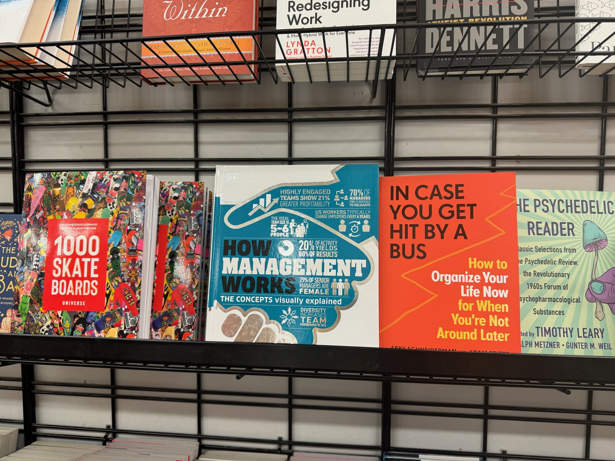 Books are displayed on a metal shelf, including titles about skateboards, management, life organization, and psychedelic reading.