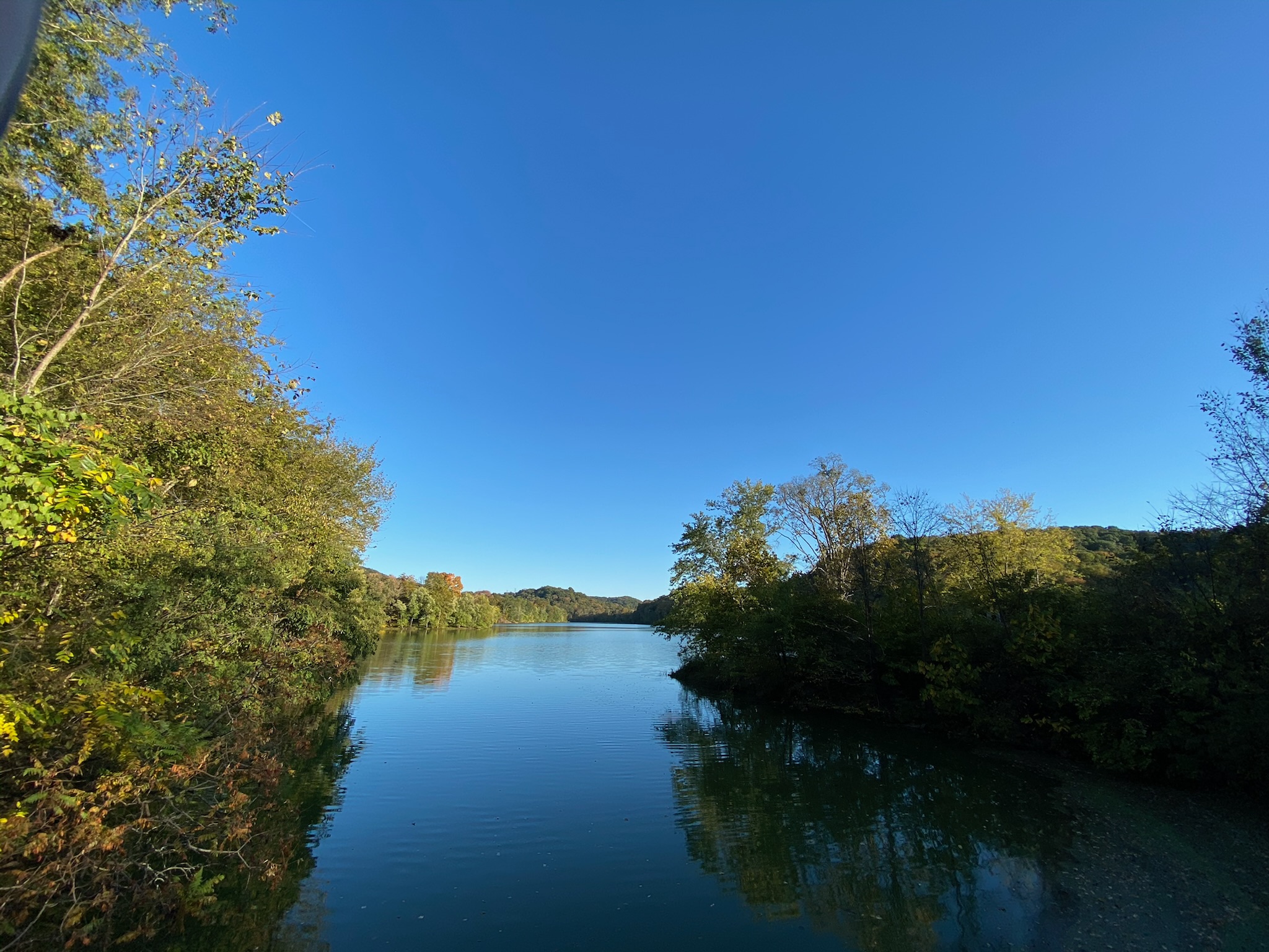A calm river bordered by dense green trees reflects the clear blue sky on a sunny day near Nashville.