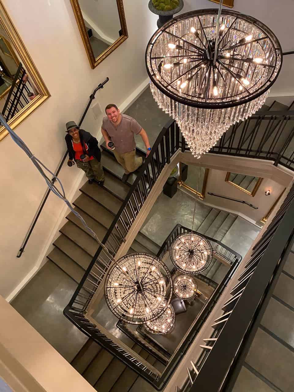 View from above of two people on a Nashville staircase, with elegant chandeliers and mirrors decorating the walls.