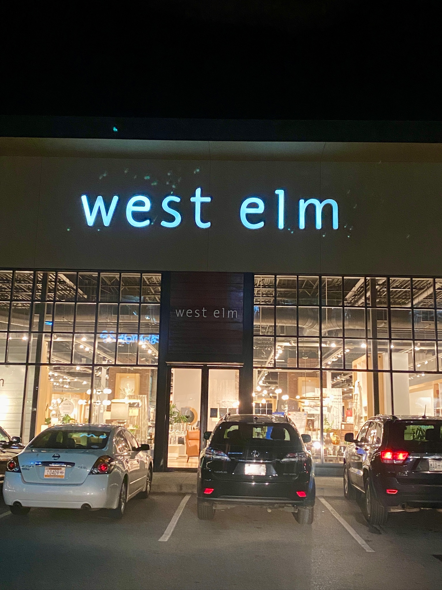 Three cars are parked in front of a well-lit West Elm store in Nashville at night, with the store's illuminated sign visible above the entrance.