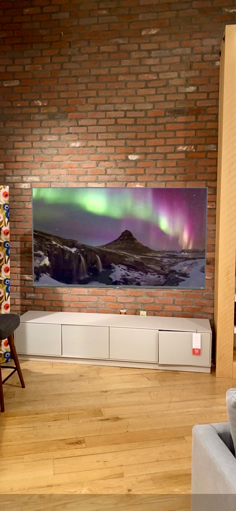 A large flat-screen TV on a low white console displays an image of the northern lights against a brick wall in a modern Nashville living room.