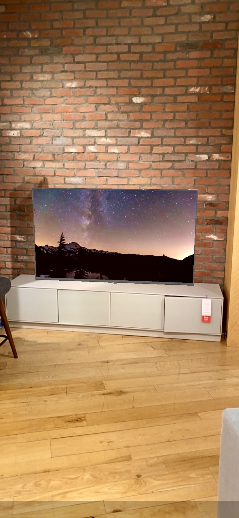 A flat-screen TV displaying a starry night scene sits on a low white cabinet against a brick wall on a wooden floor, bringing Nashville charm into the cozy living space.