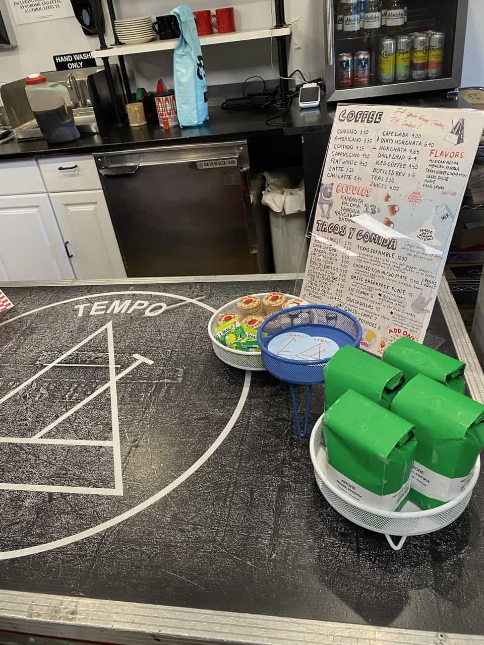 Counter with a 'Tempo' logo, set in the vibrant heart of Nashville, featuring a menu displaying coffee and taco options, assorted bakery items in a basket, and green packaged goods on a dish.