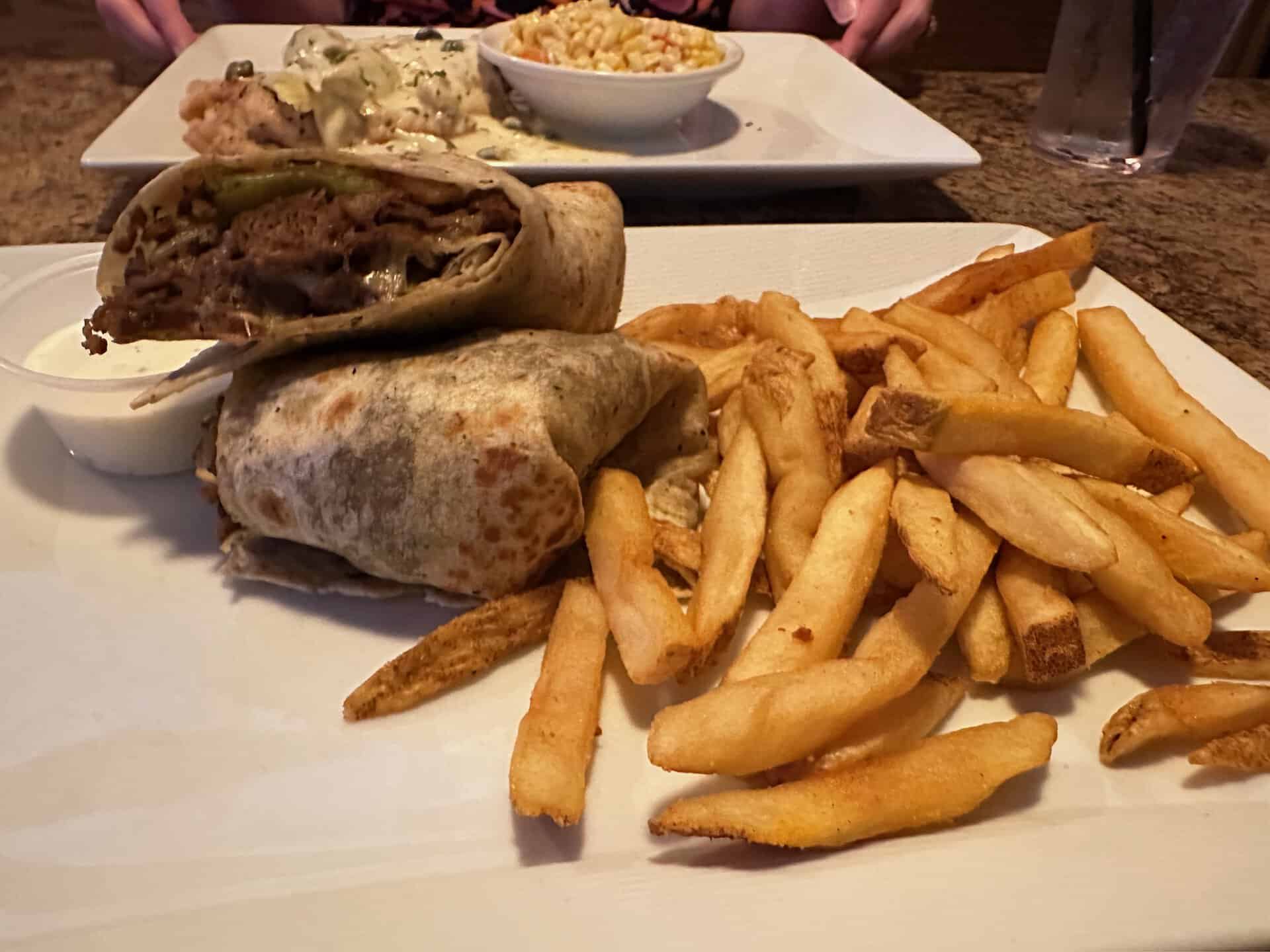 A Nashville-style beef-stuffed wrap sits next to a pile of fries on a white plate. In the background, a plate with macaroni and gravy-covered meat is partially visible, adding to the Southern charm.
