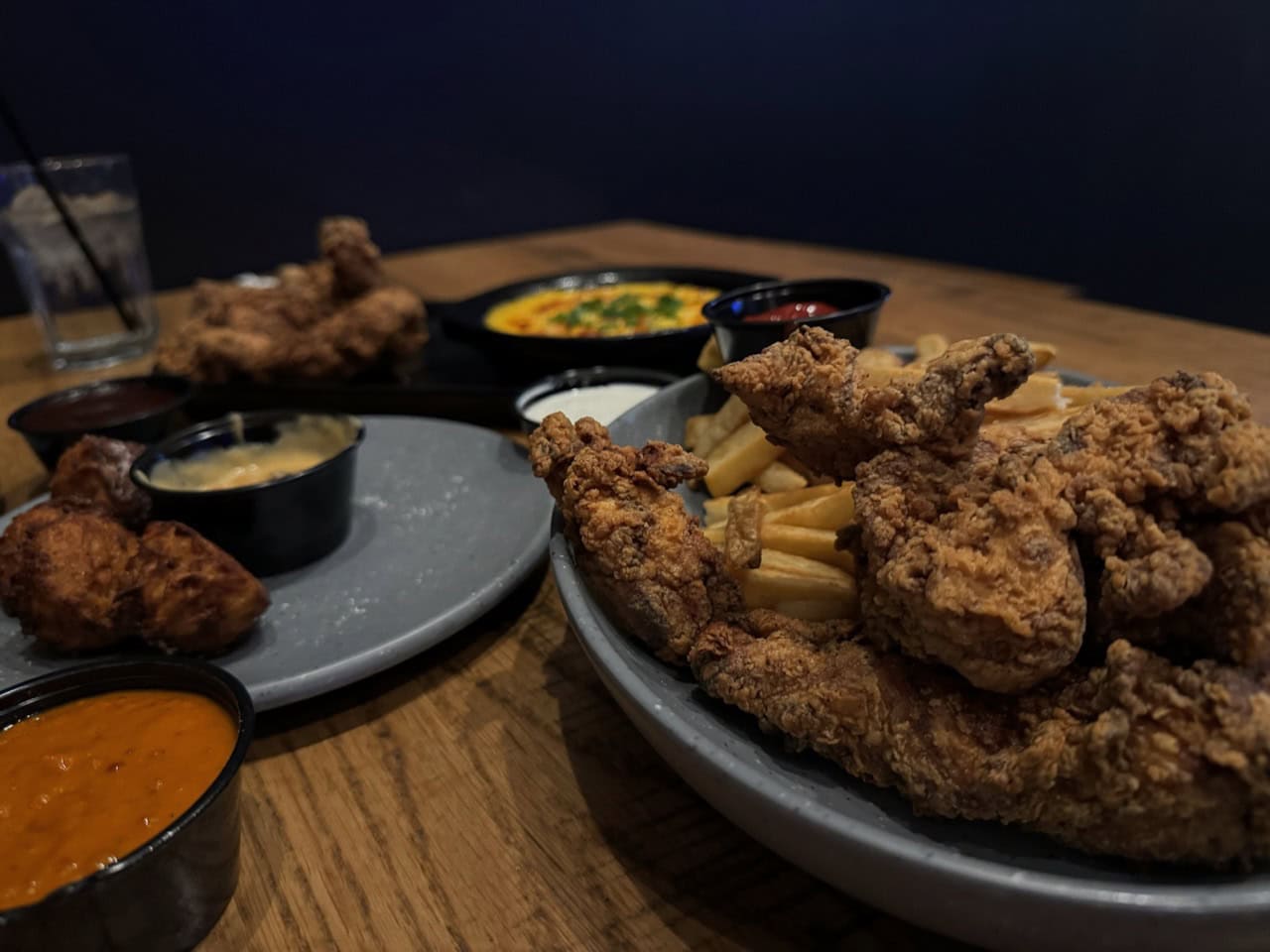Plates of Nashville fried chicken, crispy fries, tangy dipping sauces, and a dish of creamy pasta grace the wooden table.