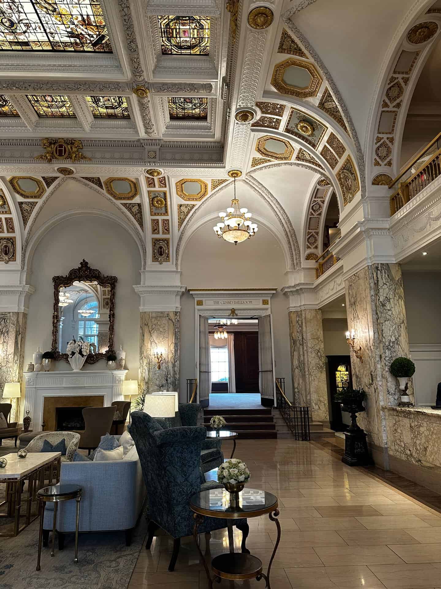 Elegant Nashville hotel lobby with ornate ceiling, stained glass details, chandeliers, and marble columns. Plush seating areas with sofas and chairs around small tables.