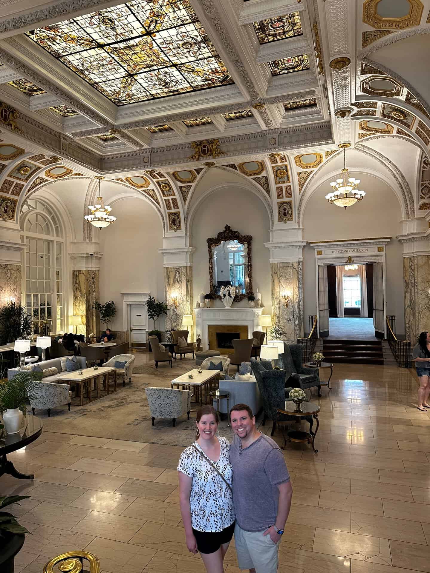 A couple stands in a luxurious Nashville hotel lobby, surrounded by ornate ceilings, stained glass, and plush seating.