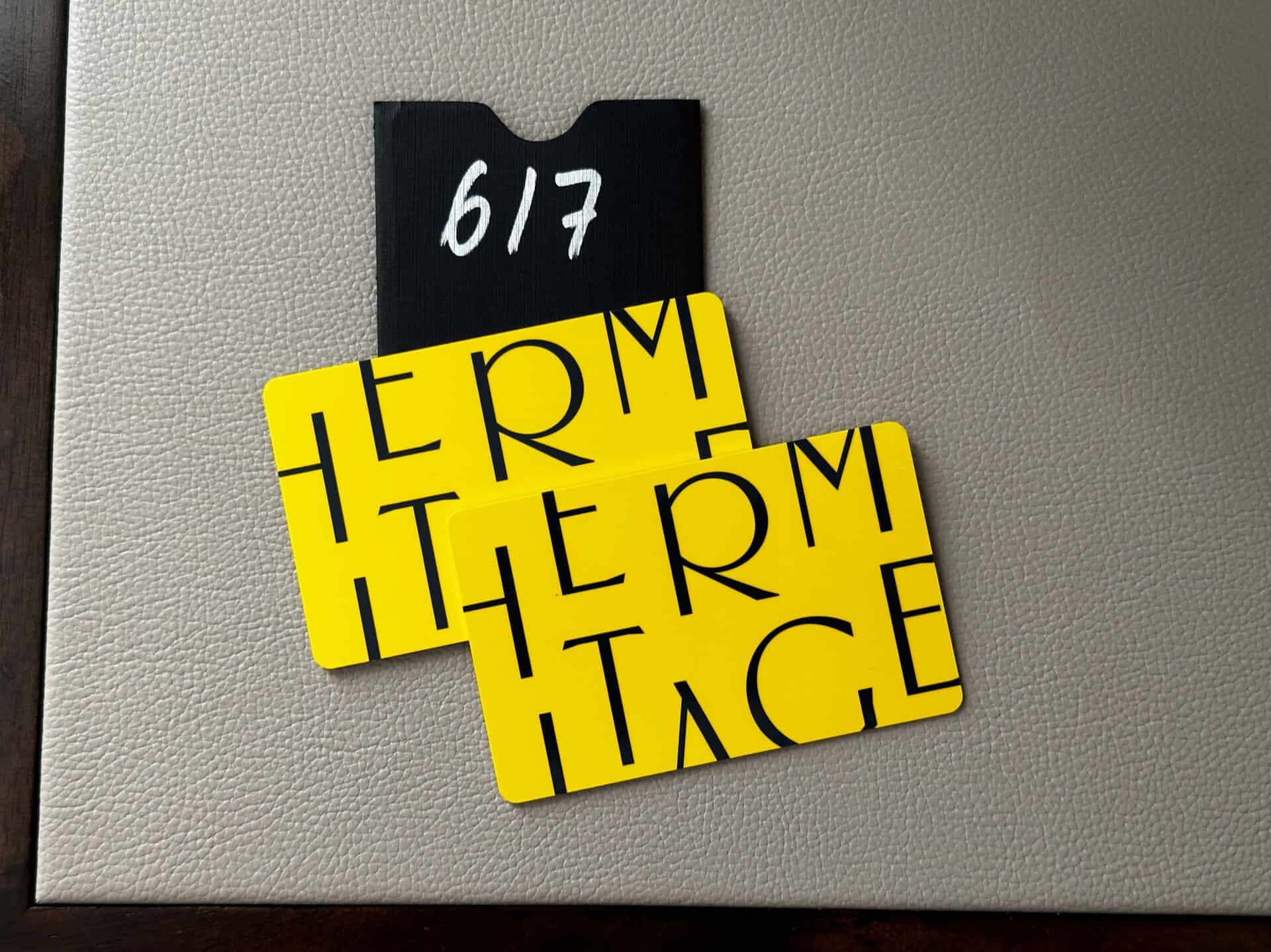 Two yellow hotel key cards with "Hermitage" text rest on a gray surface. A black holder showcasing "617" peeks from behind the cards, revealing a touch of Nashville charm.