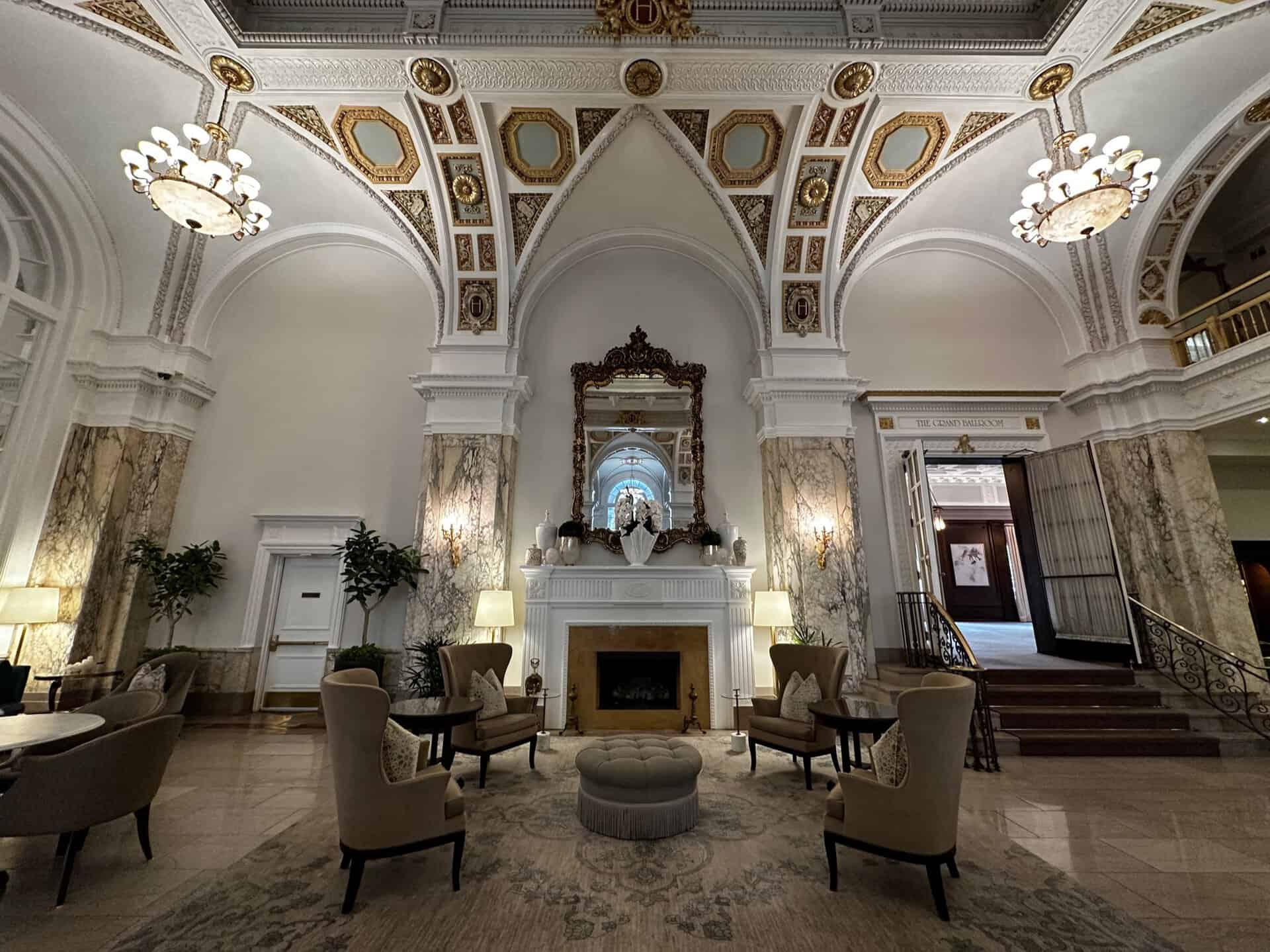 In the heart of Nashville, this elegant hotel lobby boasts ornate arched ceilings, chandeliers, and marble columns. A large decorative mirror sits above a fireplace, while arranged seating in neutral tones invites guests to relax in refined comfort.