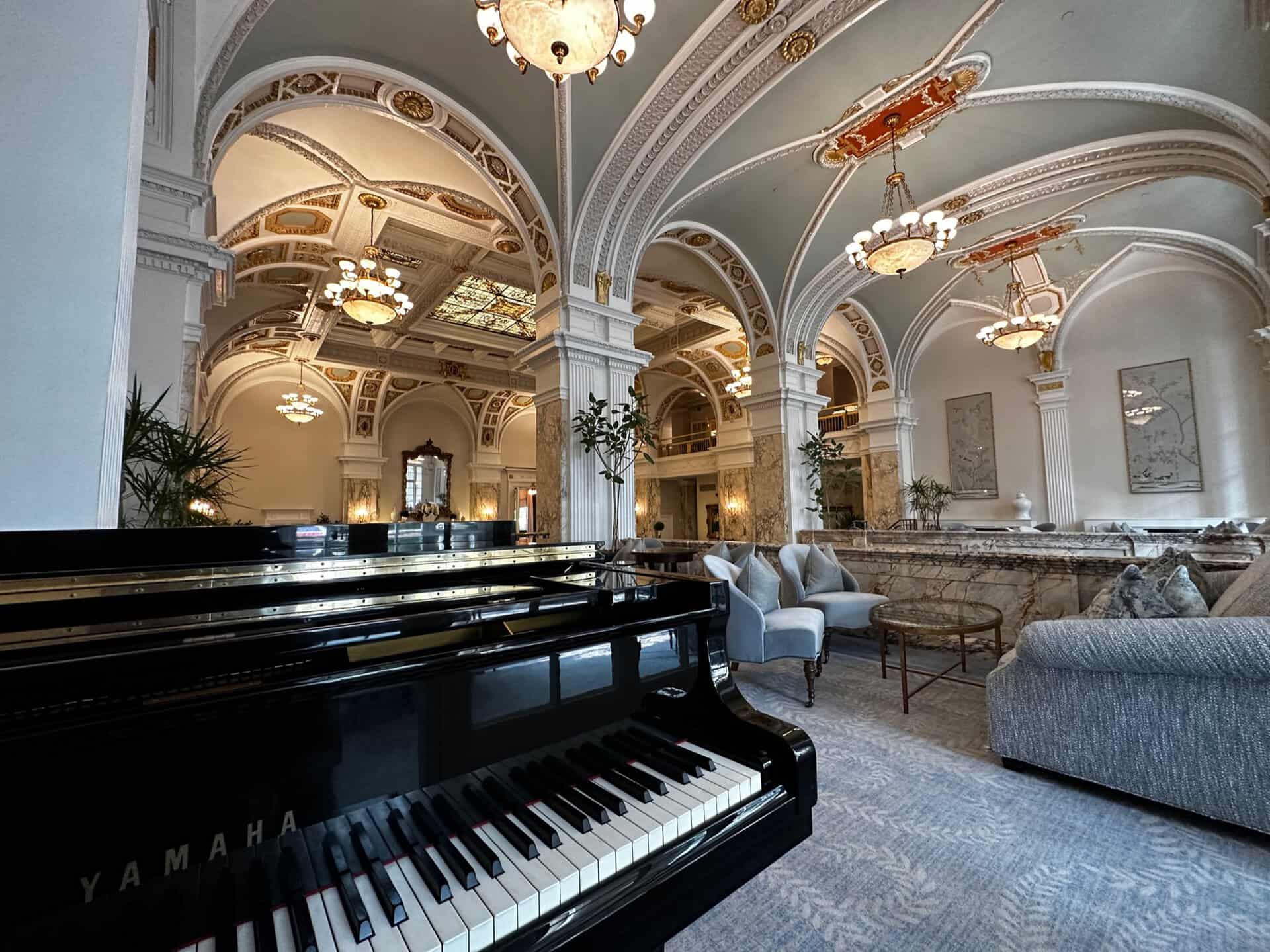 The Nashville hotel lobby exudes elegance with its ornate ceiling, chandeliers, and grand arches. A black Yamaha piano graces the foreground, while plush seating offers a cozy spot to unwind.