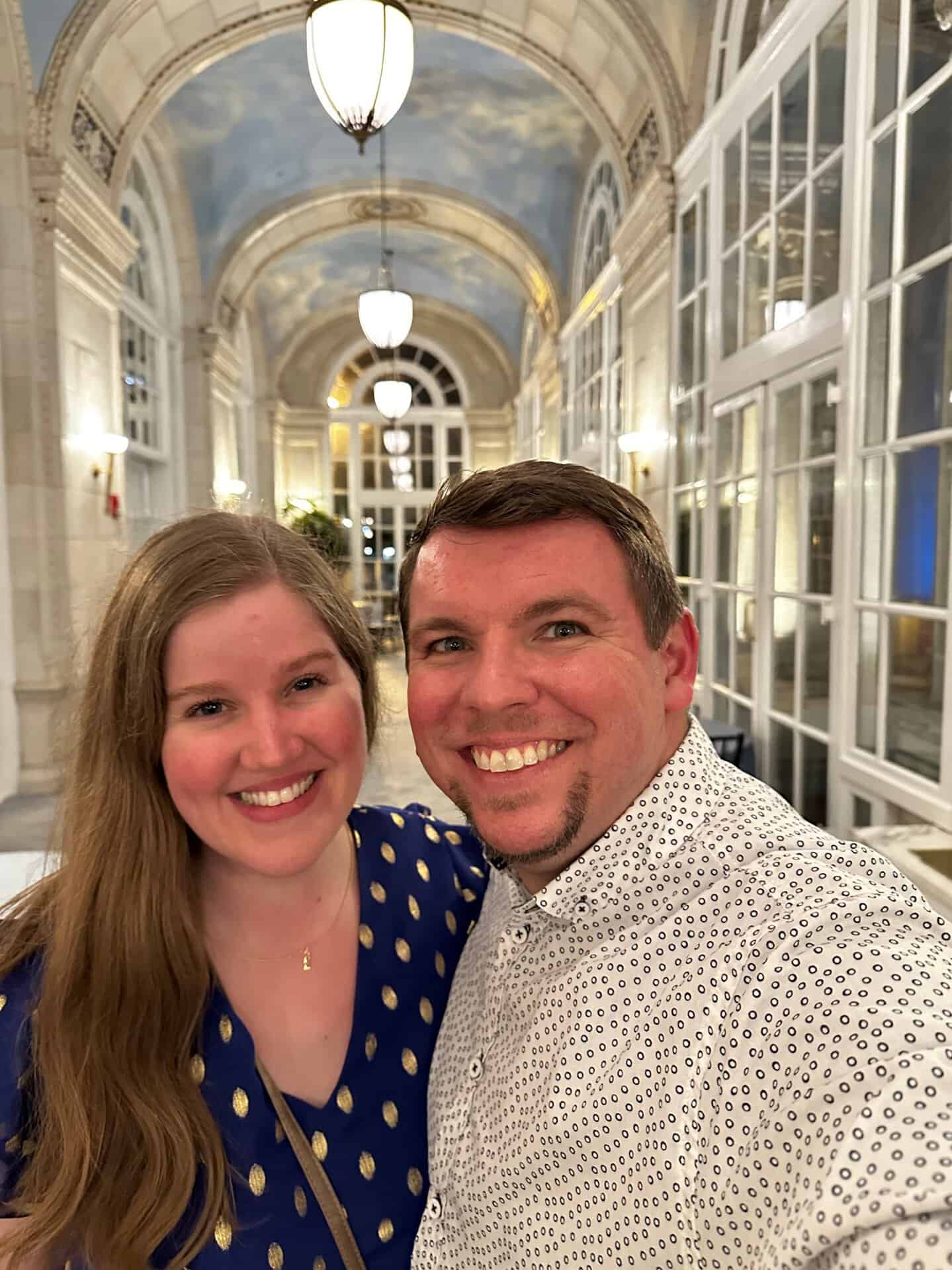 A smiling couple takes a selfie in an ornate Nashville hallway with arched windows and decorative ceilings.