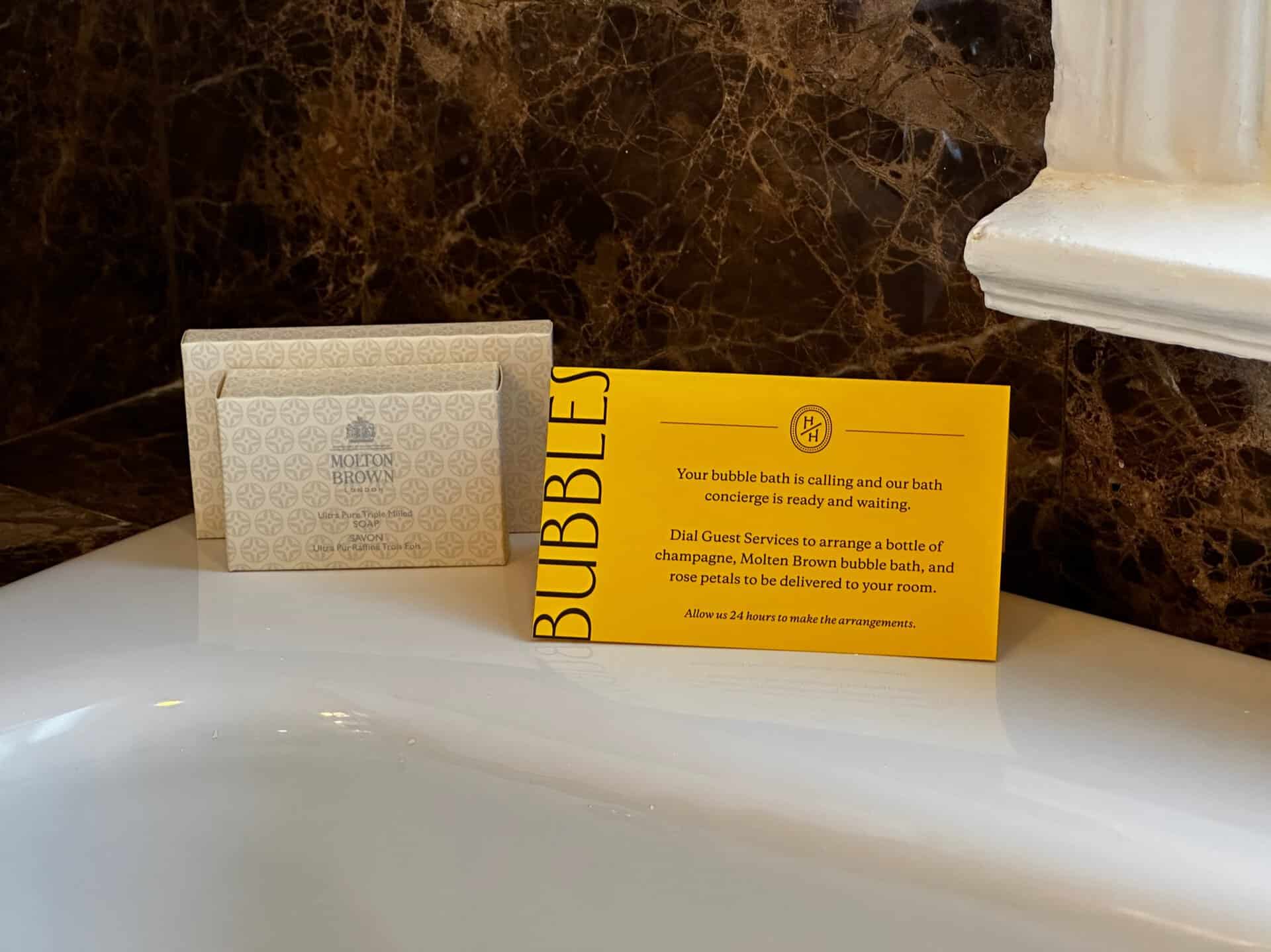 Yellow card by a bath in Nashville promotes a bubble bath and champagne service. Molton Brown bath accessories are beside it.