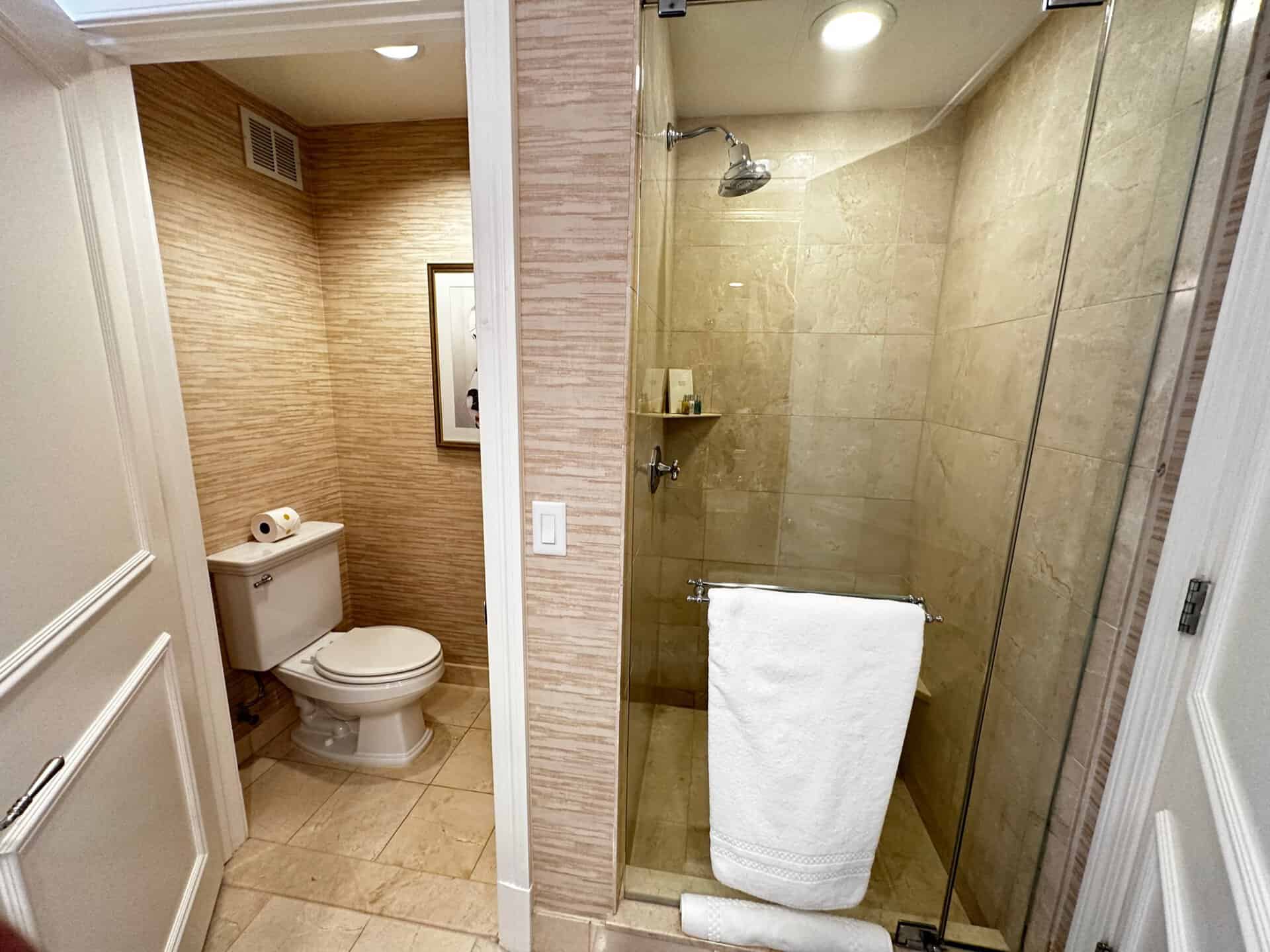 A Nashville bathroom featuring a glass-enclosed shower and white towel, complemented by a toilet with two rolls of toilet paper, all set against elegant beige tile flooring and walls.
