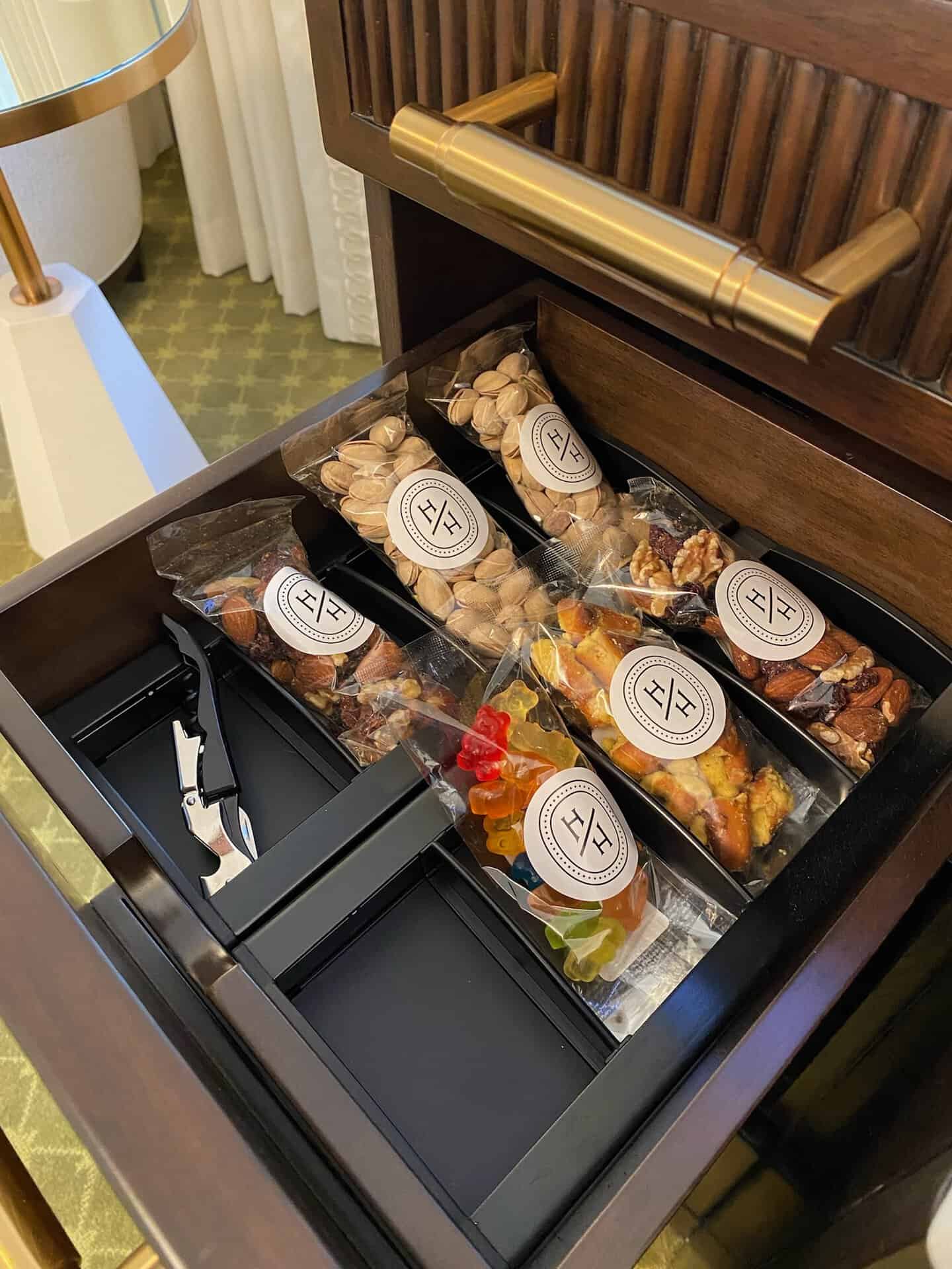 In a Nashville hotel room, a drawer reveals packaged snacks like nuts and gummy candy, nestled beside a corkscrew.