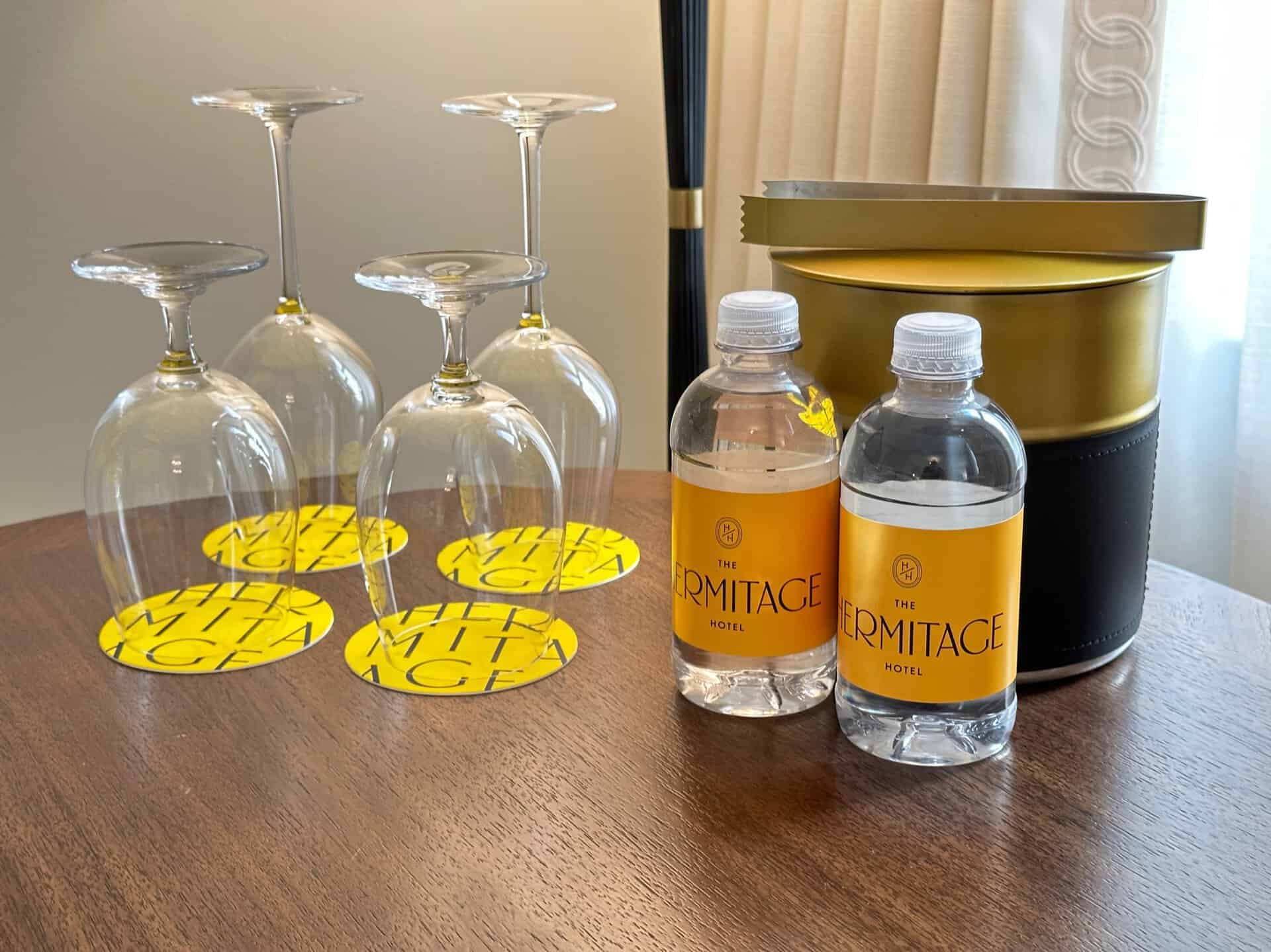 Four upside-down wine glasses rest on coasters alongside two bottles of water labeled "The Hermitage Hotel" and an ice bucket, all elegantly arranged on a wooden table—a perfect slice of Nashville hospitality.