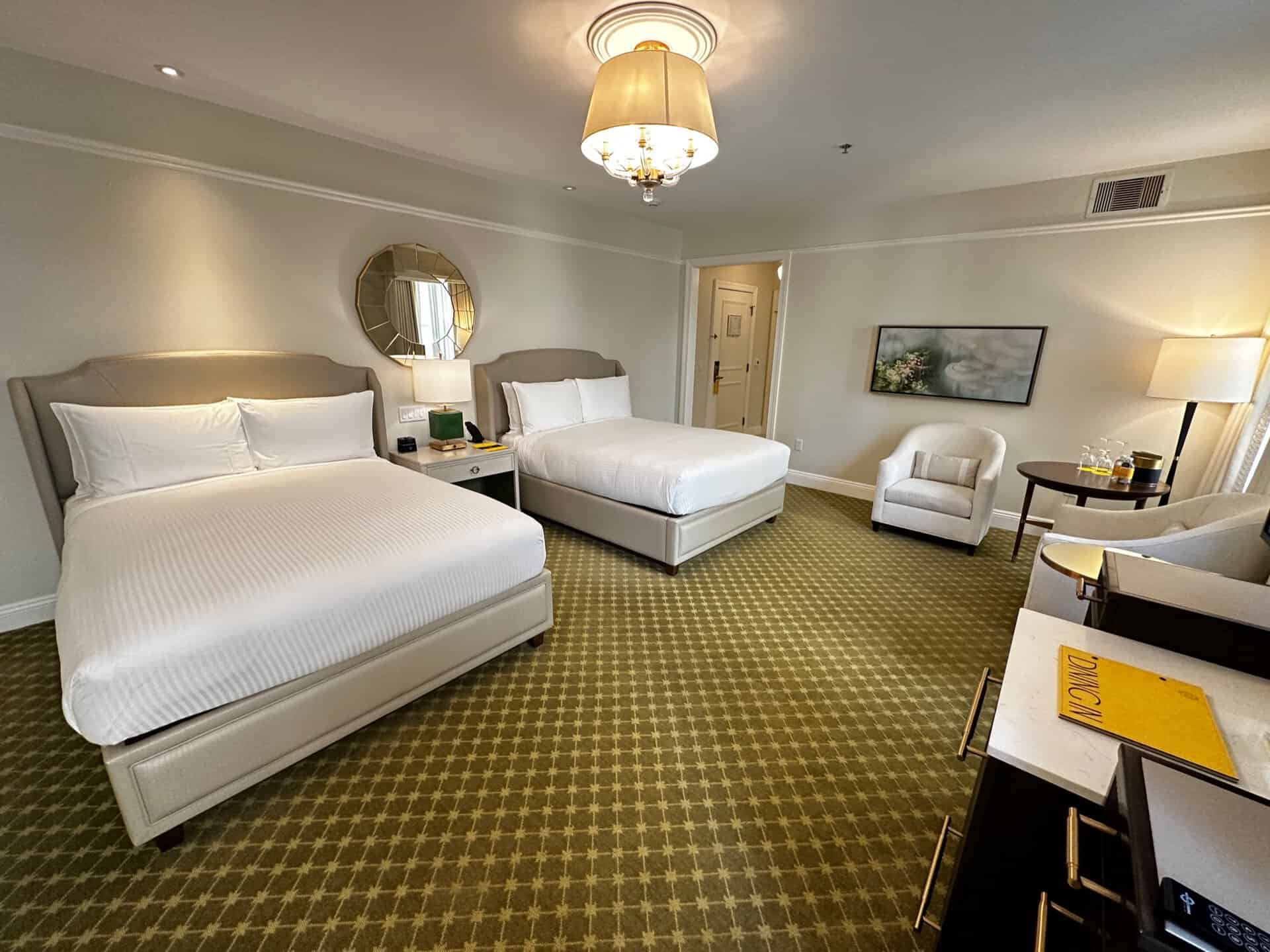 This Nashville hotel room features two double beds, a green patterned carpet, and a cozy seating area. In the foreground, you'll find a desk with a chair, while a door subtly beckons from the background, inviting exploration of Music City's vibrant spirit.