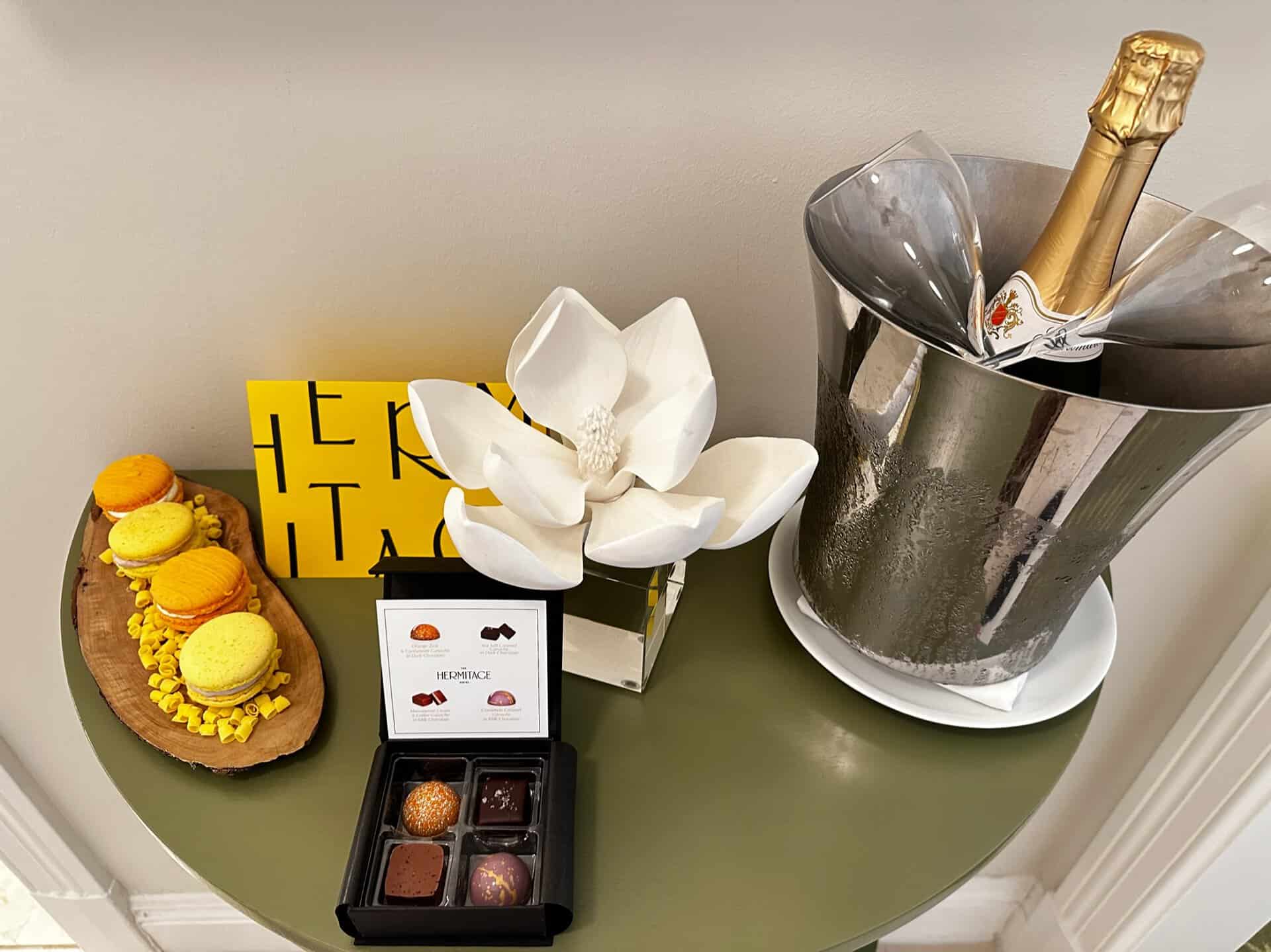 A table adorned with a Nashville flair features a decorated cake, assorted chocolates, a metal ice bucket with champagne, and a large paper flower in a vase.