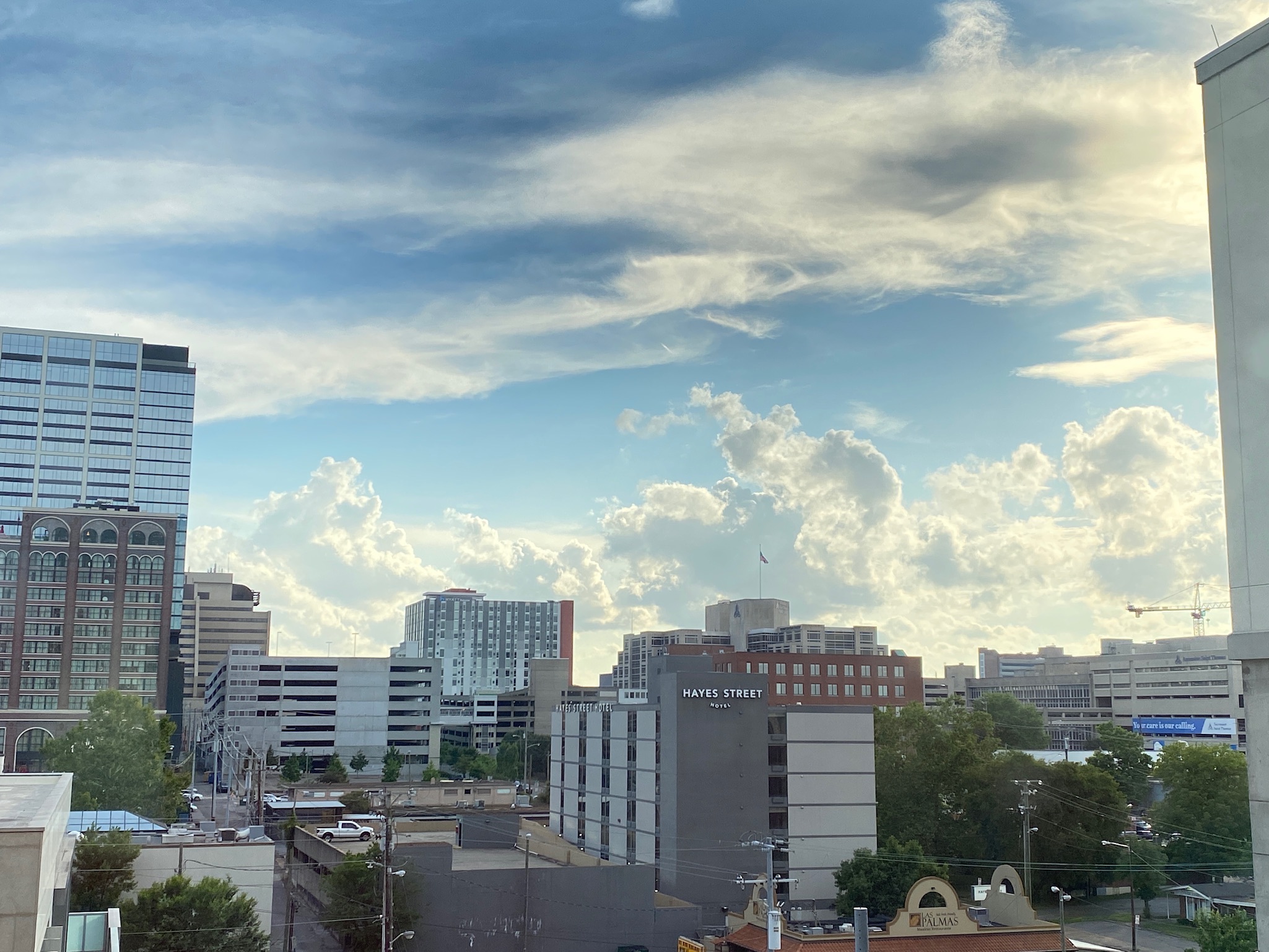 Urban skyline with mid-rise buildings, trees, and a partly cloudy sky during daytime. The "Water Street" sign is visible on one of the buildings.