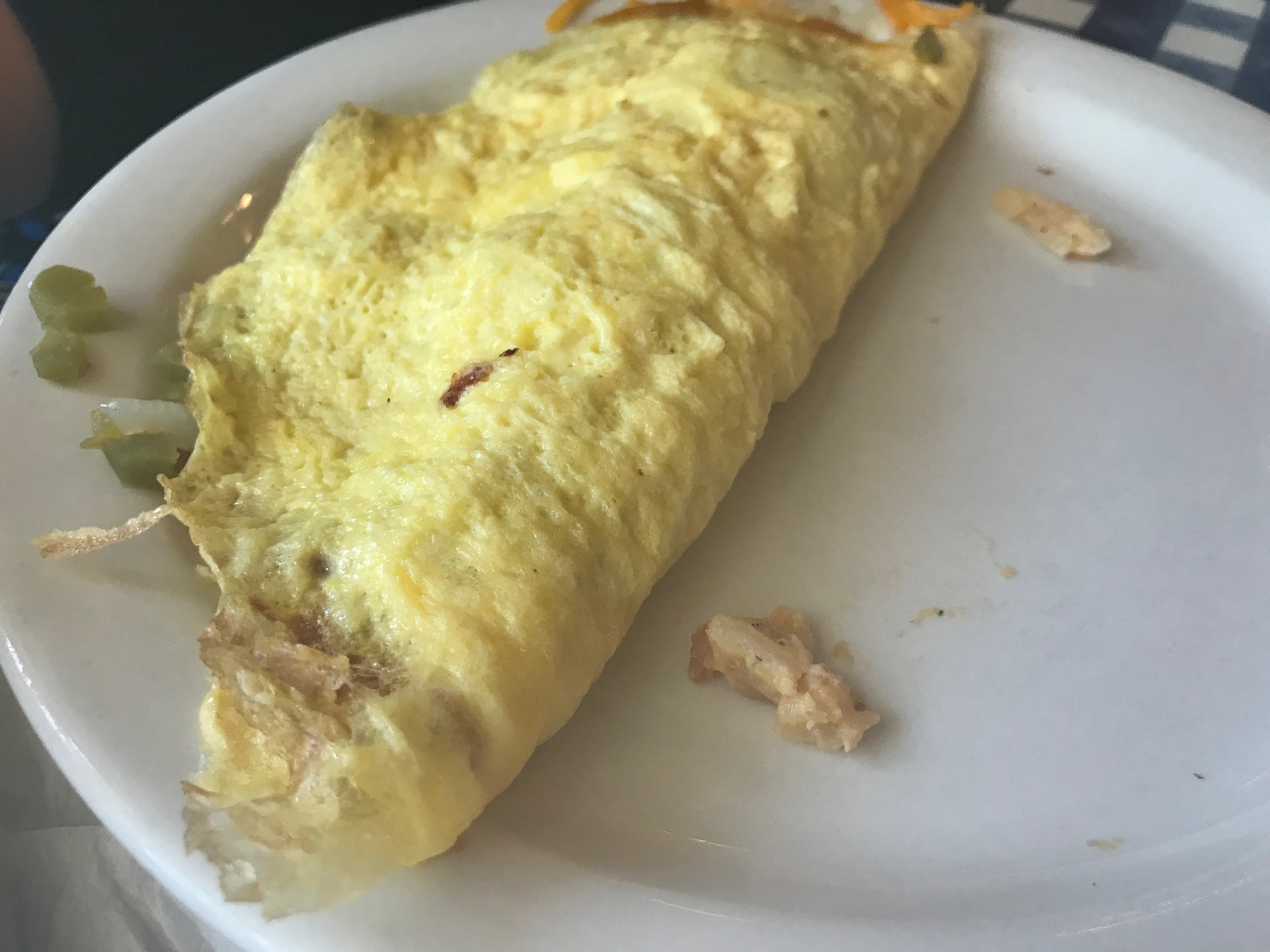 A yellow omelette on a white plate with a few small pieces of diced vegetables on the side.