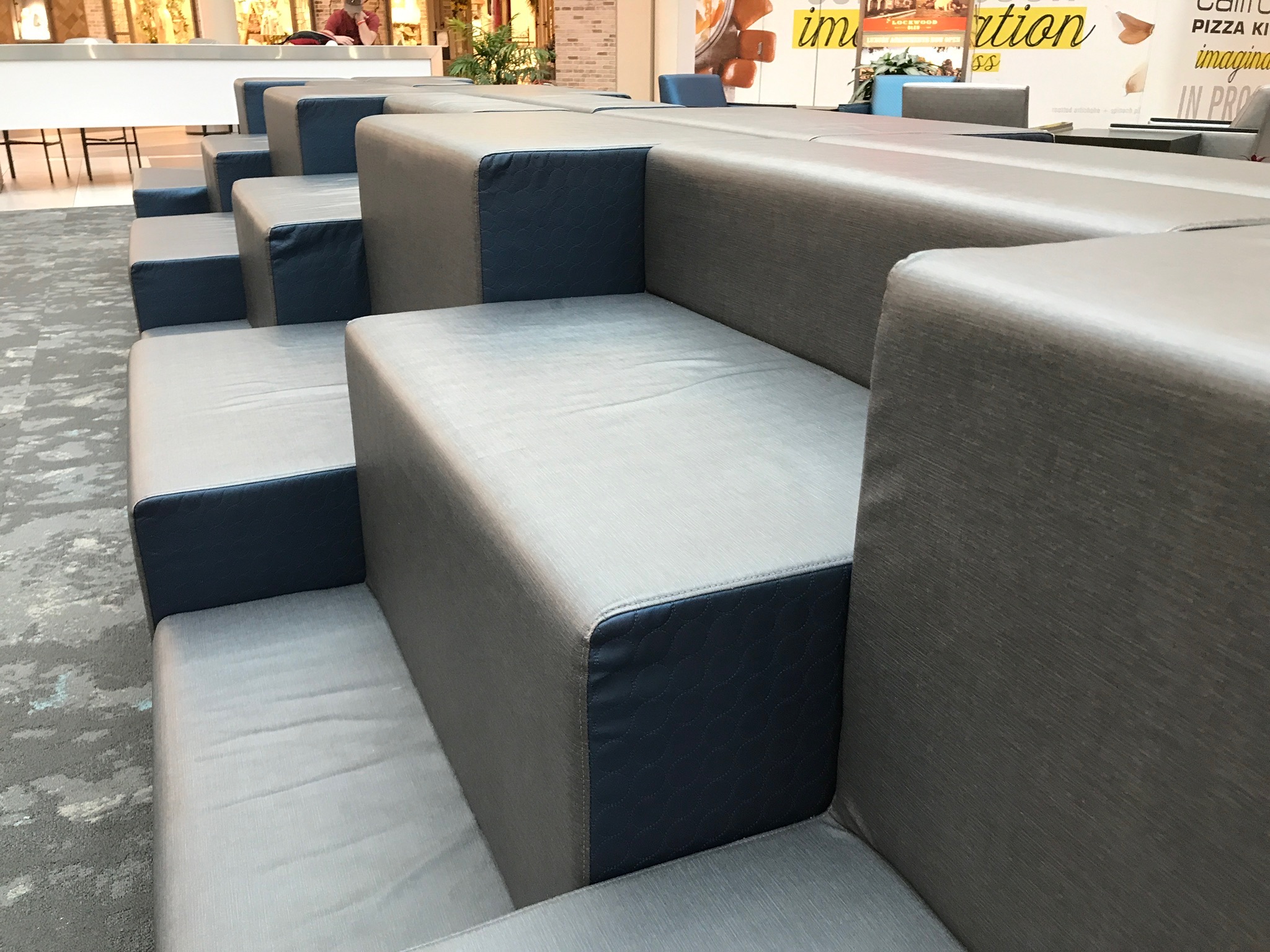 Tiered gray and blue seating with cushioned benches arranged in steps in a public indoor space.