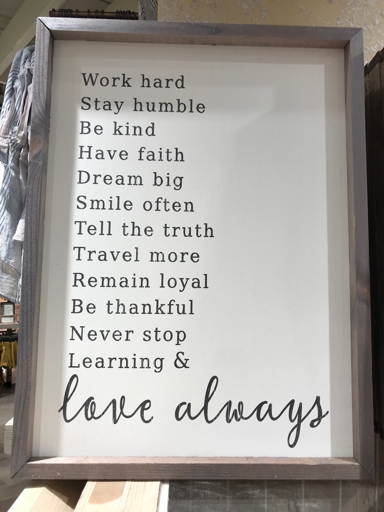 A framed sign listing positive life advice such as "Work hard," "Stay humble," "Dream big," and ending with "love always" in cursive at the bottom.