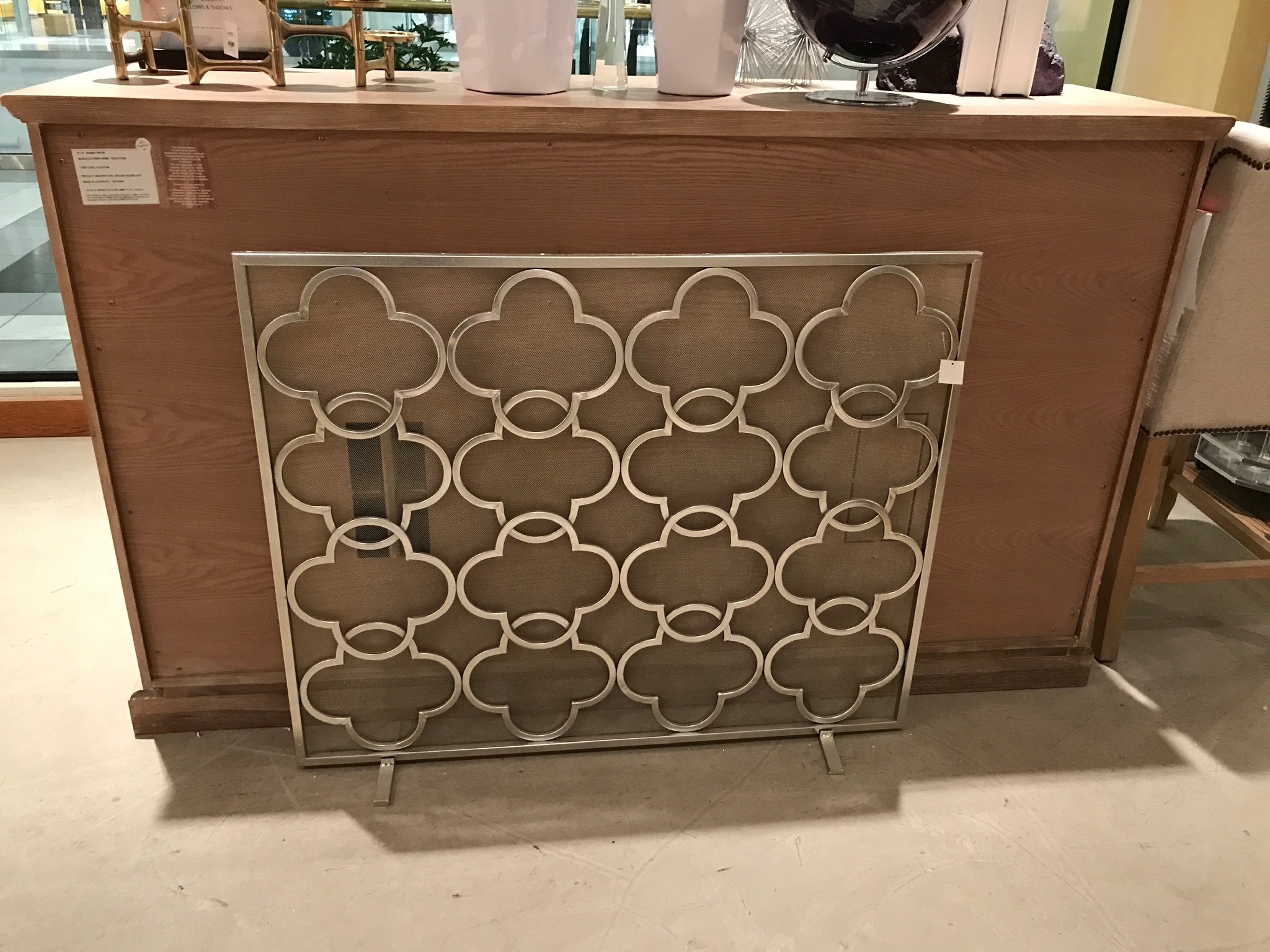 A decorative metal panel with a repeating quatrefoil pattern is displayed in front of a wooden counter in a store.