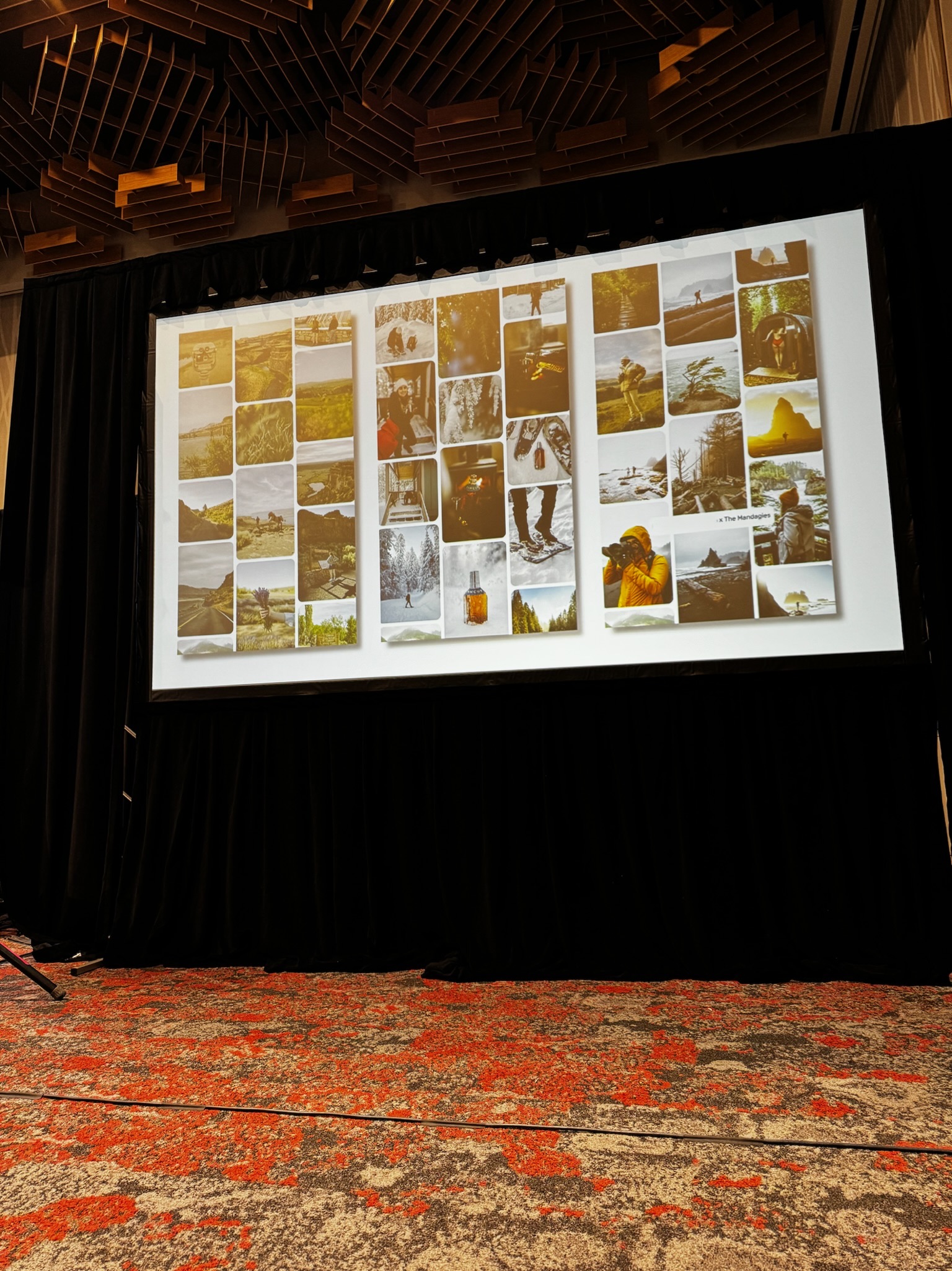 A large projection screen displays a grid of outdoor and adventure photographs in a conference room with a patterned carpet and dark drapes.