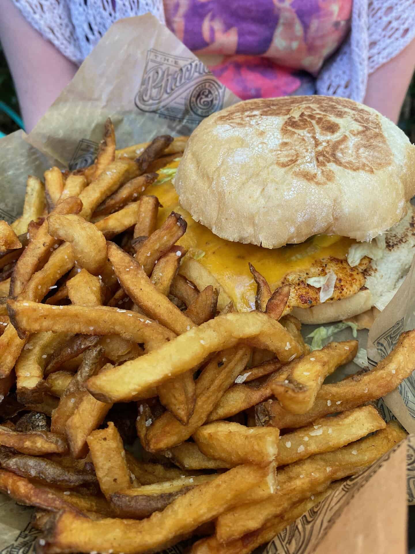 Burger with melted cheese on a toasted bun, served with a side of golden-brown fries on wax paper.