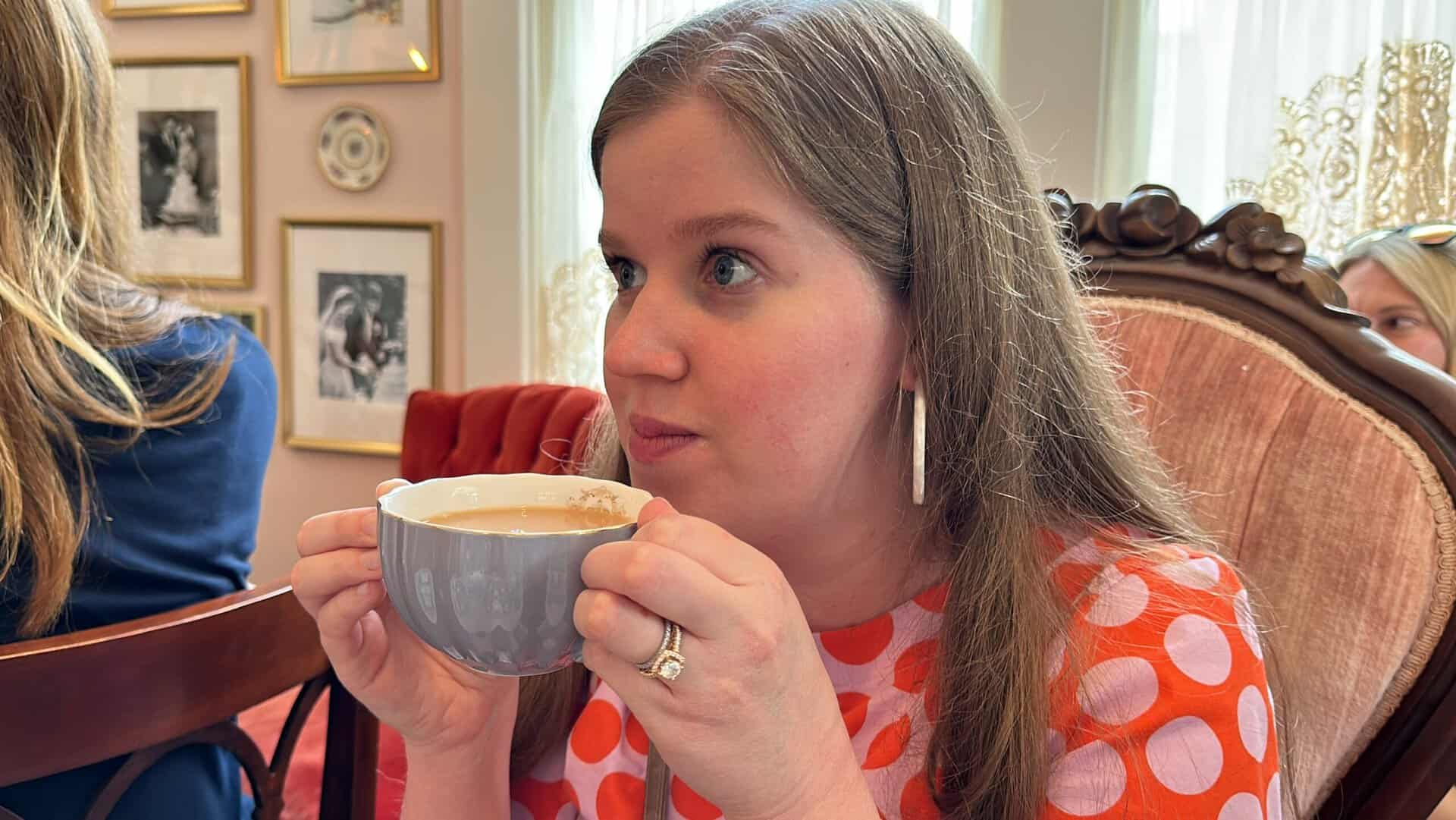 In a warmly decorated Nashville room adorned with framed pictures, a woman with long hair sips from a gray cup, wearing her vibrant red polka dot shirt.