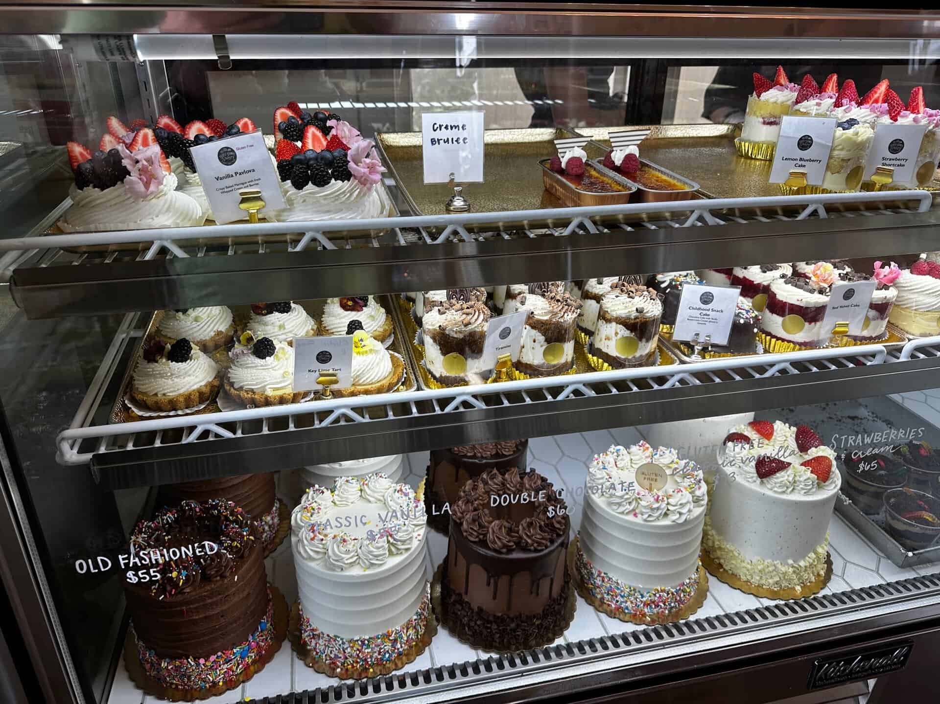 A display case in Nashville showcases assorted cakes and cupcakes, featuring chocolate and vanilla varieties. Each treat is neatly labeled with a price and description, capturing the Southern charm in every bite.