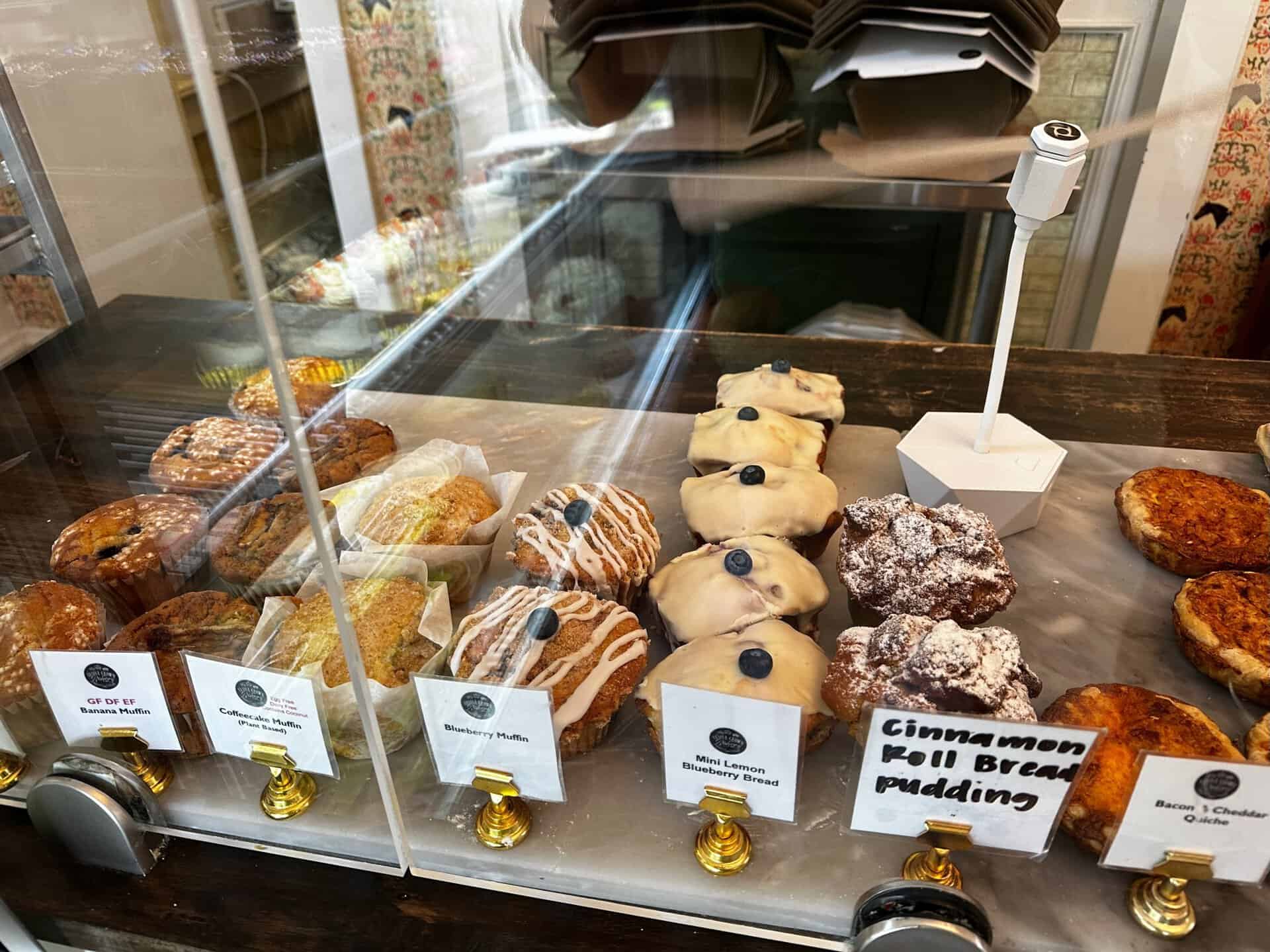 A display case in Nashville showcases a variety of pastries, including muffins, lemon bread, and cinnamon roll bread pudding, all neatly labeled behind a clear barrier.