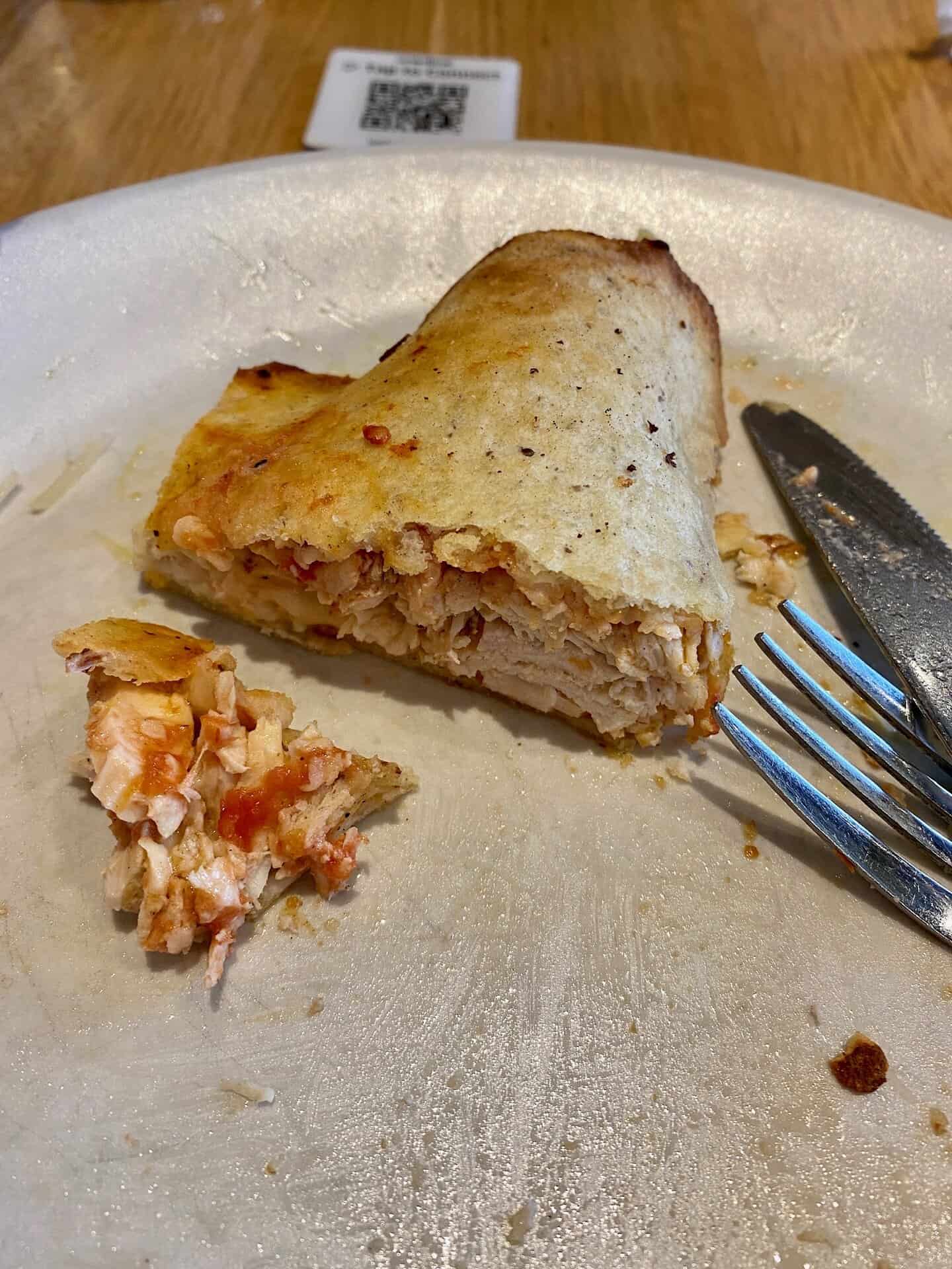 Partially eaten calzone on a white plate, with a fork and knife beside it. A QR code is visible in the background.
