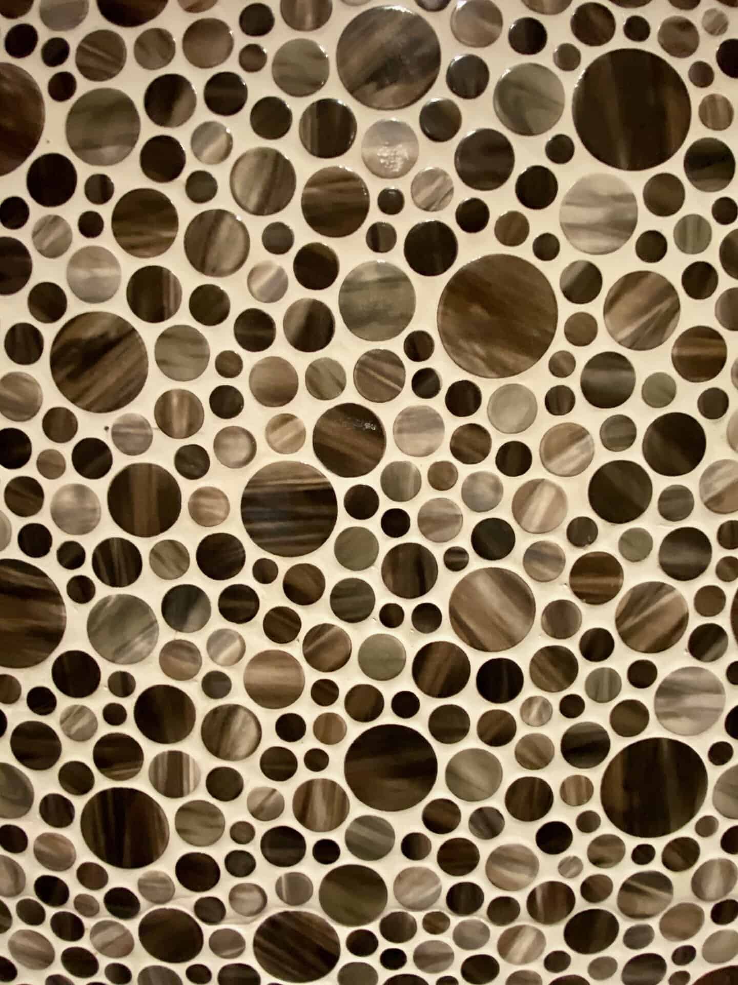 A pattern of round, textured tiles in varying sizes and shades of brown and gray, arranged on a light-colored surface.