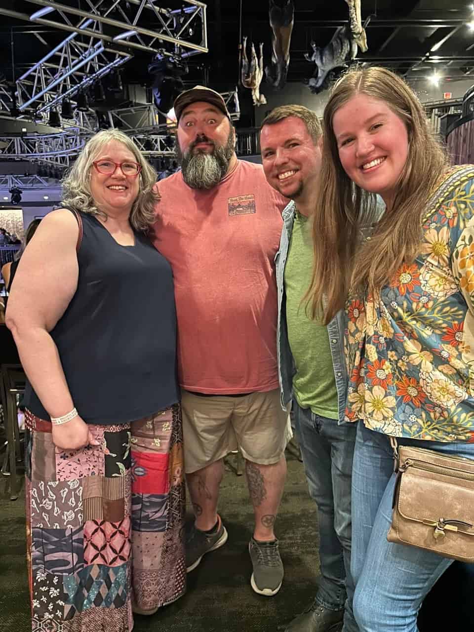 Four people standing indoors in Nashville, smiling at the camera. The setting includes a ceiling with metal beams and some charming decorations.